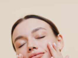 Young woman applying cosmetic white cream on face